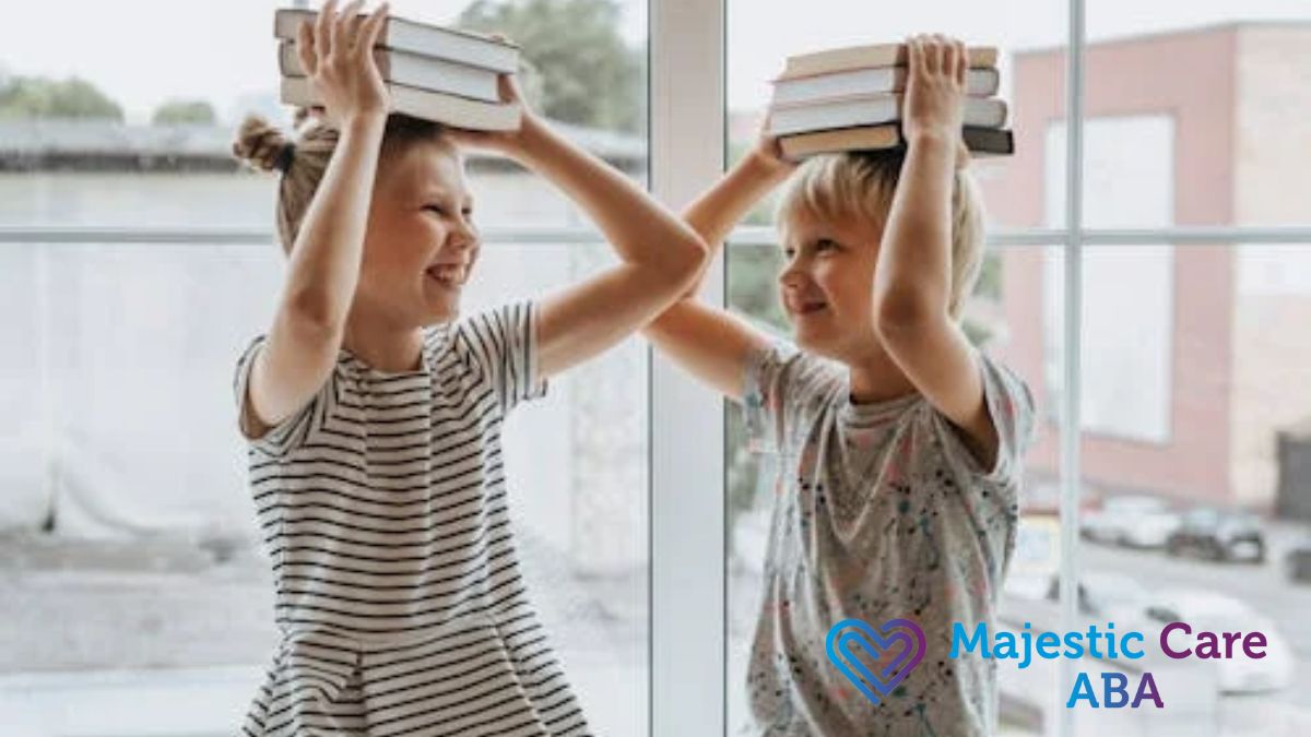 A boy and a girl balance books on their heads while sitting on a sunny window sill.