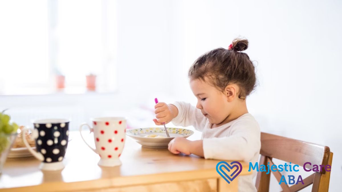 A young girl in profile eats independently at a kitchen table.
