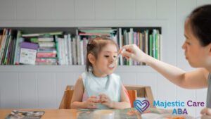 A young girl is spoon-fed by her mother, appearing receptive to the food.
