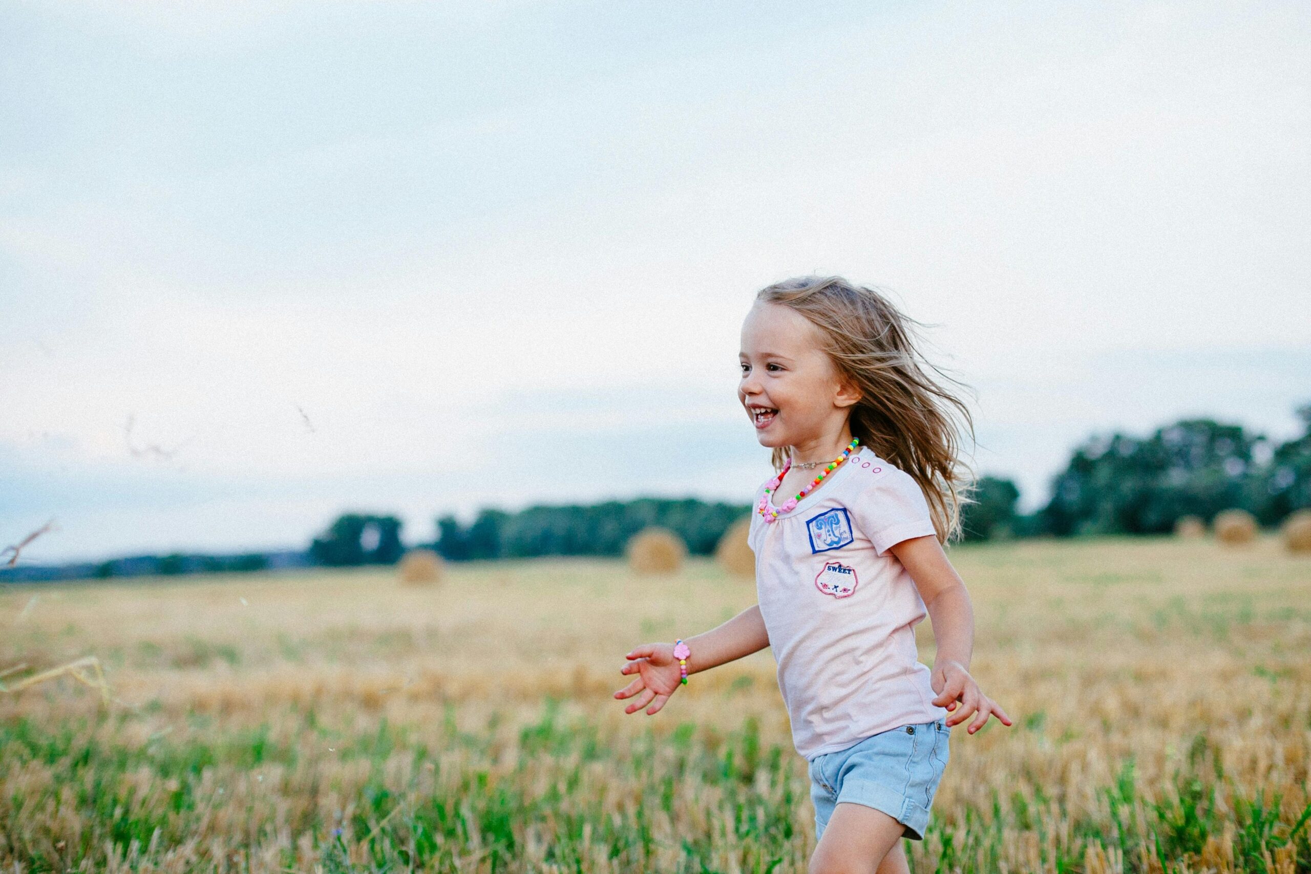 Young girl in a shirt and shorts running across a sunlit meadow.