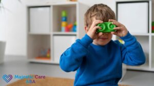 Young boy in a blue sweatshirt at a center-based ABA therapy session, playfully looking through toy blocks like a telescope.