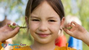 Young girl in an orange dress during an ABA therapy session, smiling at the camera while balancing flowers behind her ears.