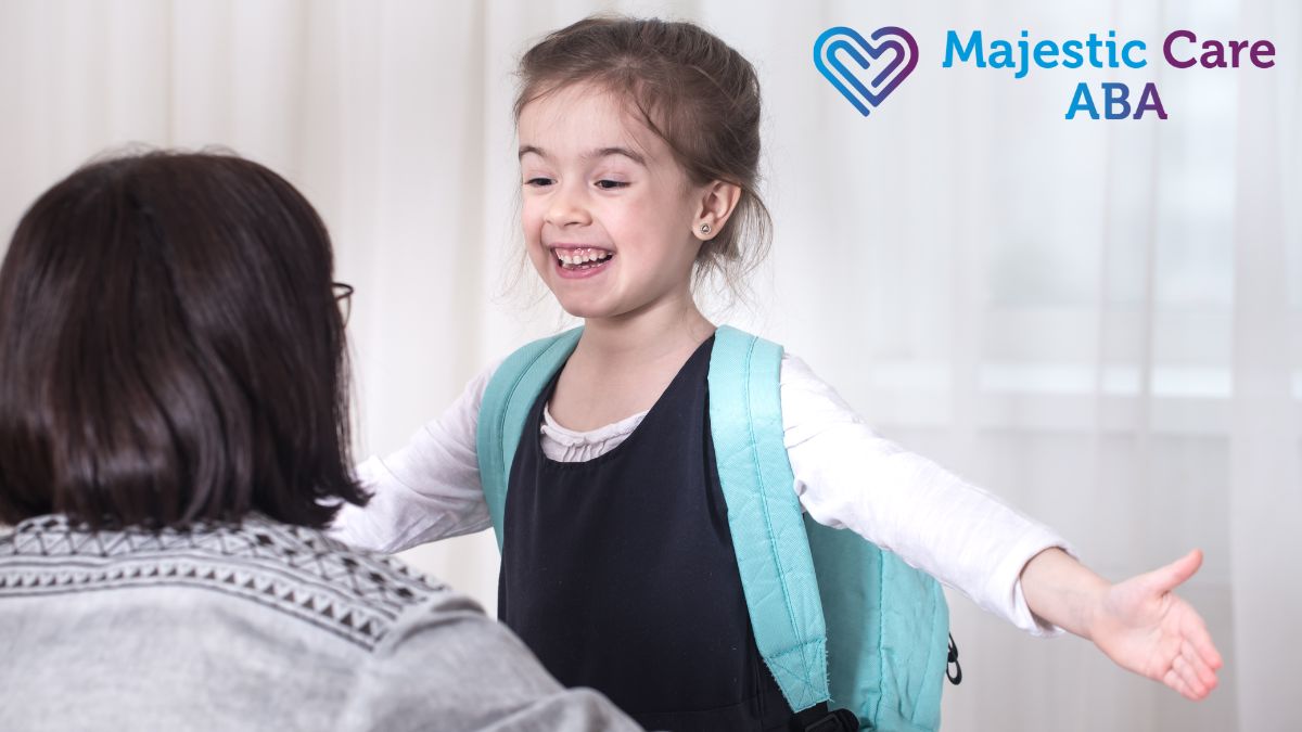 A young girl spreads her arms out in joy while being encouraged by a therapist during an autism intervention session.
