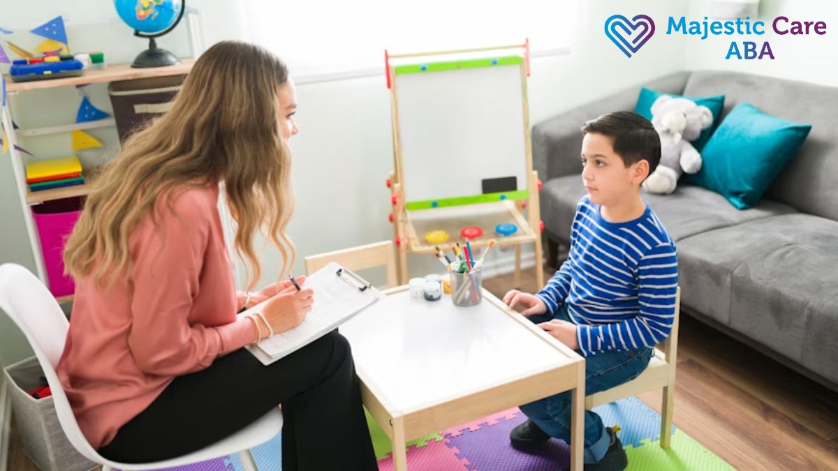 ABA therapy session, a female therapist talks with a young boy in a classroom to check how he is doing.