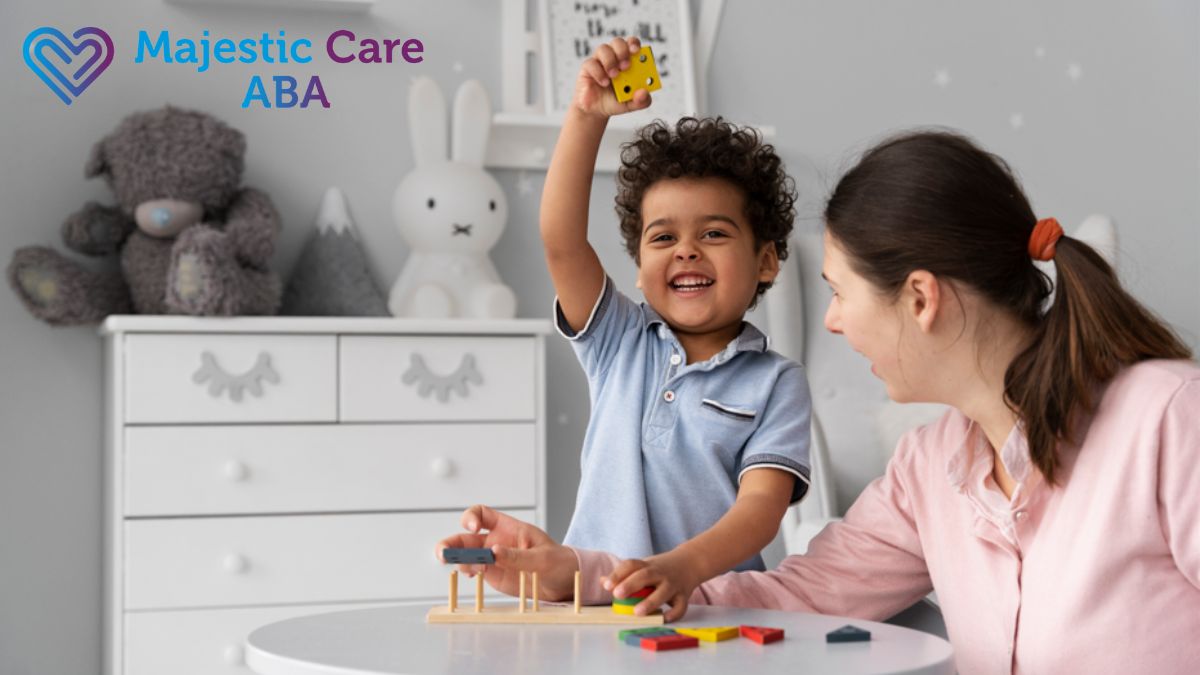 ABA therapy session with a female therapist cheering on a young boy as he plays a building blocks game at a table.