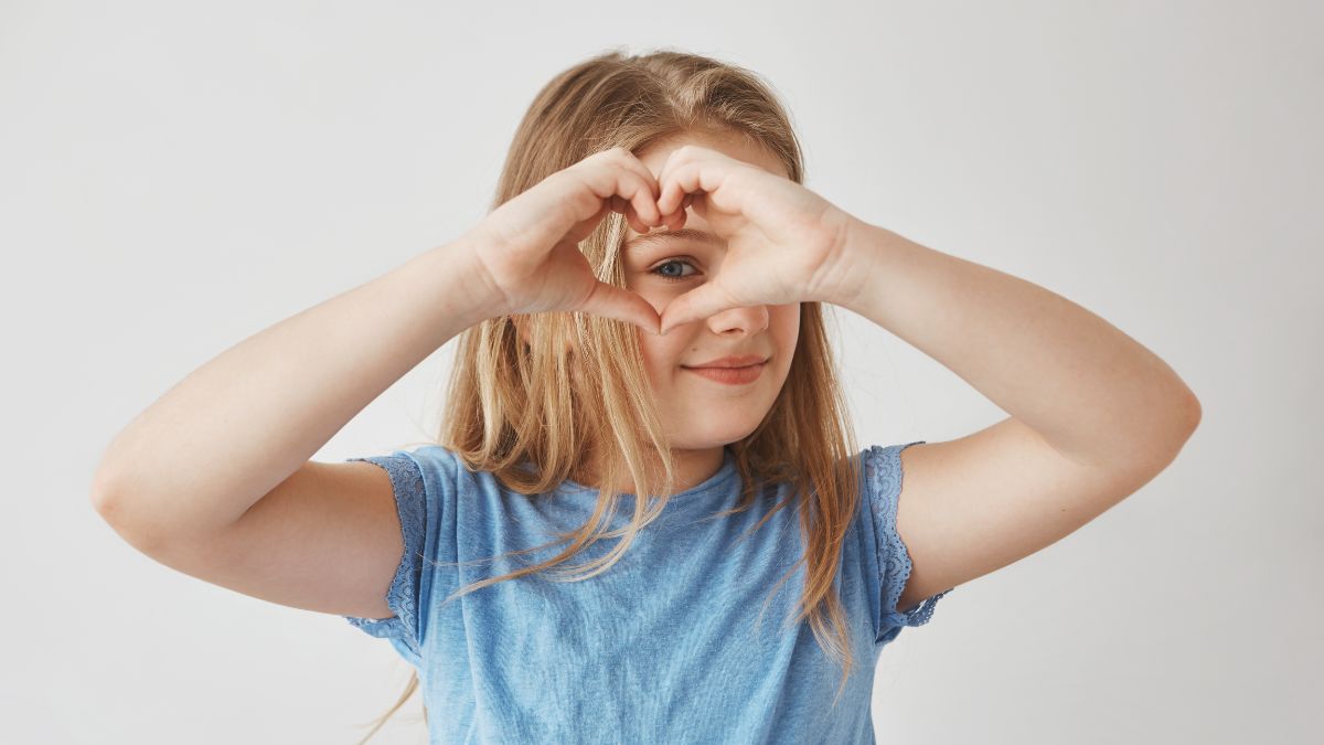 Blonde girl playfully looking through her hands shaped like a telescope.