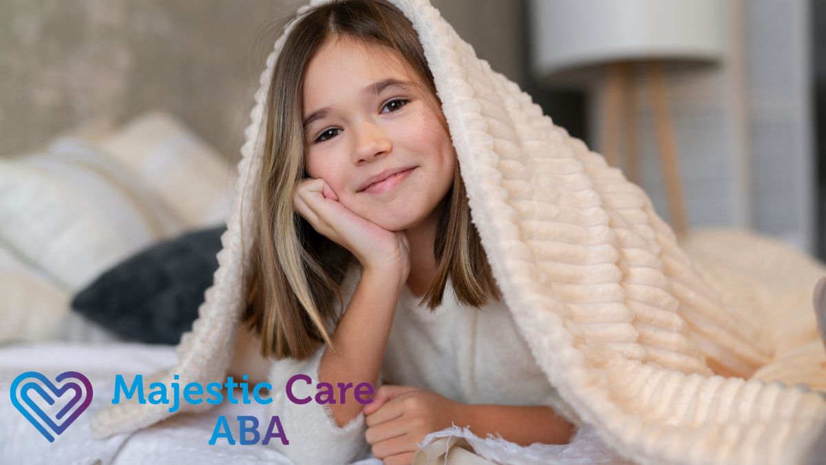 A young girl with autism smiles at the camera as she settles on a bed, wrapped head to toe in a heavy weighted blanket.