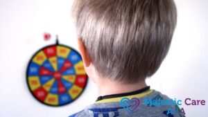 A boy with autism, showing visual sensory issues, stands with his back to the camera while focusing on a circular target board on the wall.