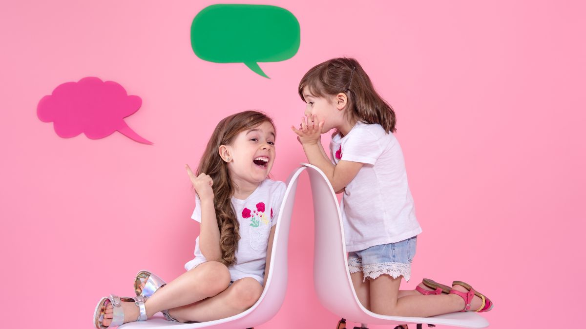 Two children in a pink room enjoying a conversation, with illustrated talk bubbles above them, demonstrating verbal behavior in ABA.