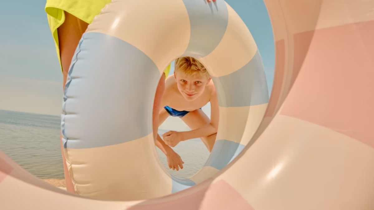A boy with autism, experiencing visual sensory issues, steps into a spiral of colorful flotation devices arranged on the beach.