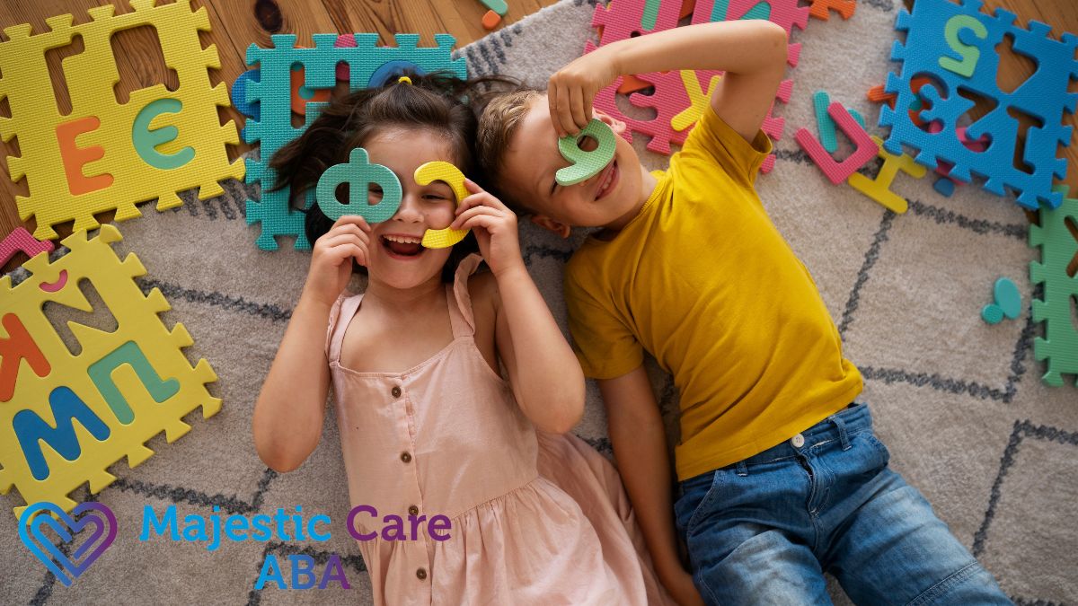 A boy and a girl lie on the floor, looking through colorful rubber toy letters with happy, joyful expressions during an ABA therapy for kids session.